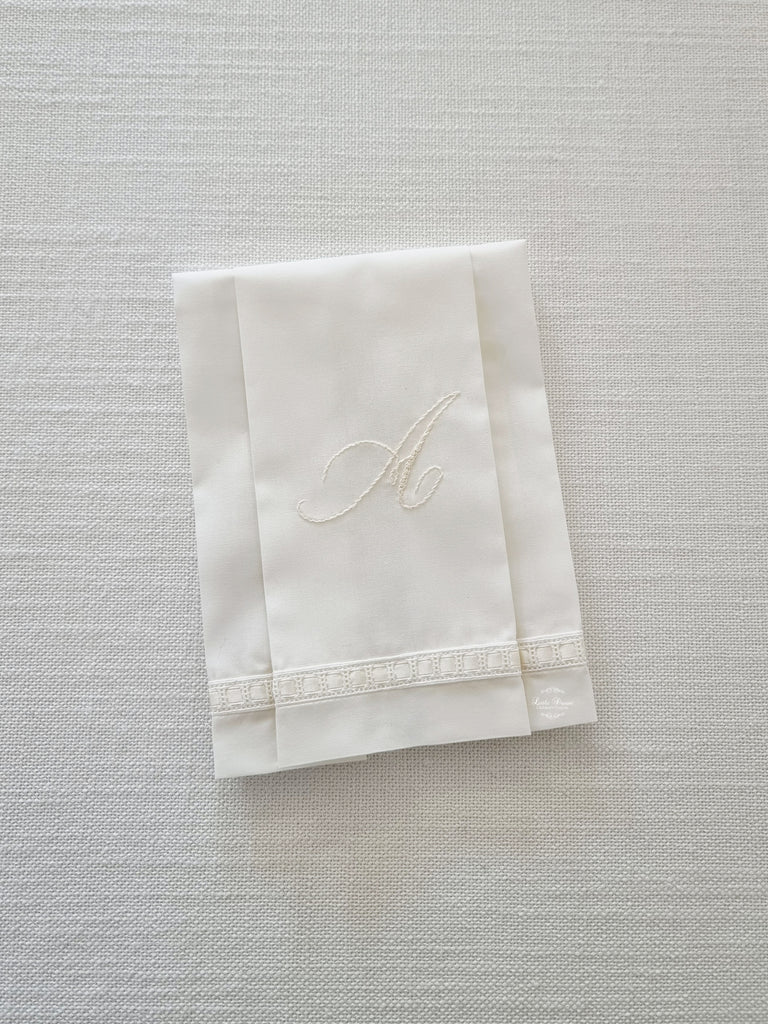 Hand made white cotton cloth with a hand embroidered initial and embellished with ribbon. Used for a Baptism sacrament. 