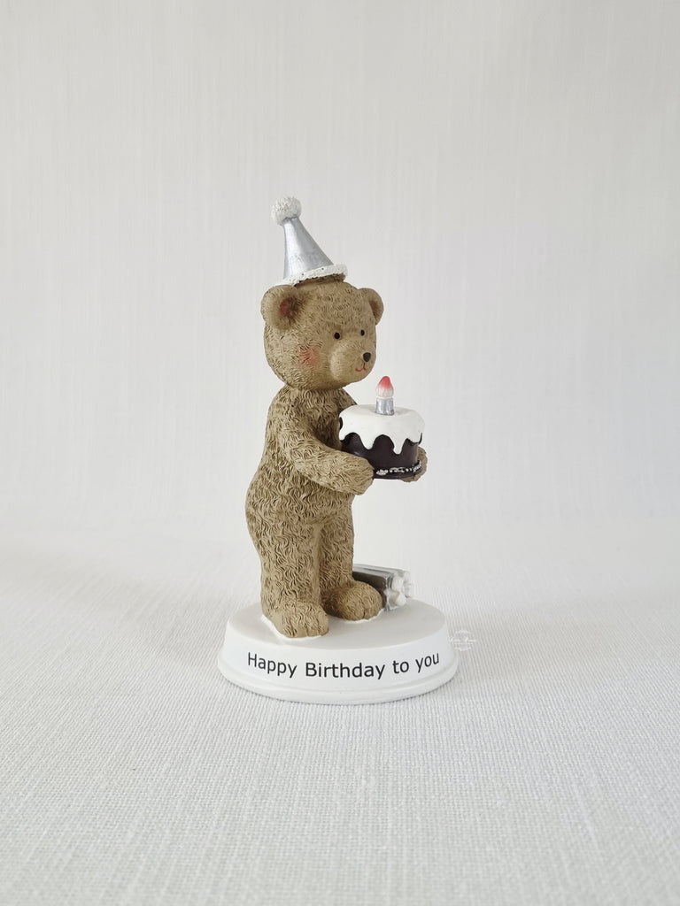 Teddy bear figurine with a birthday cake and candle on a white base with 'Happy Birthday to you' text.